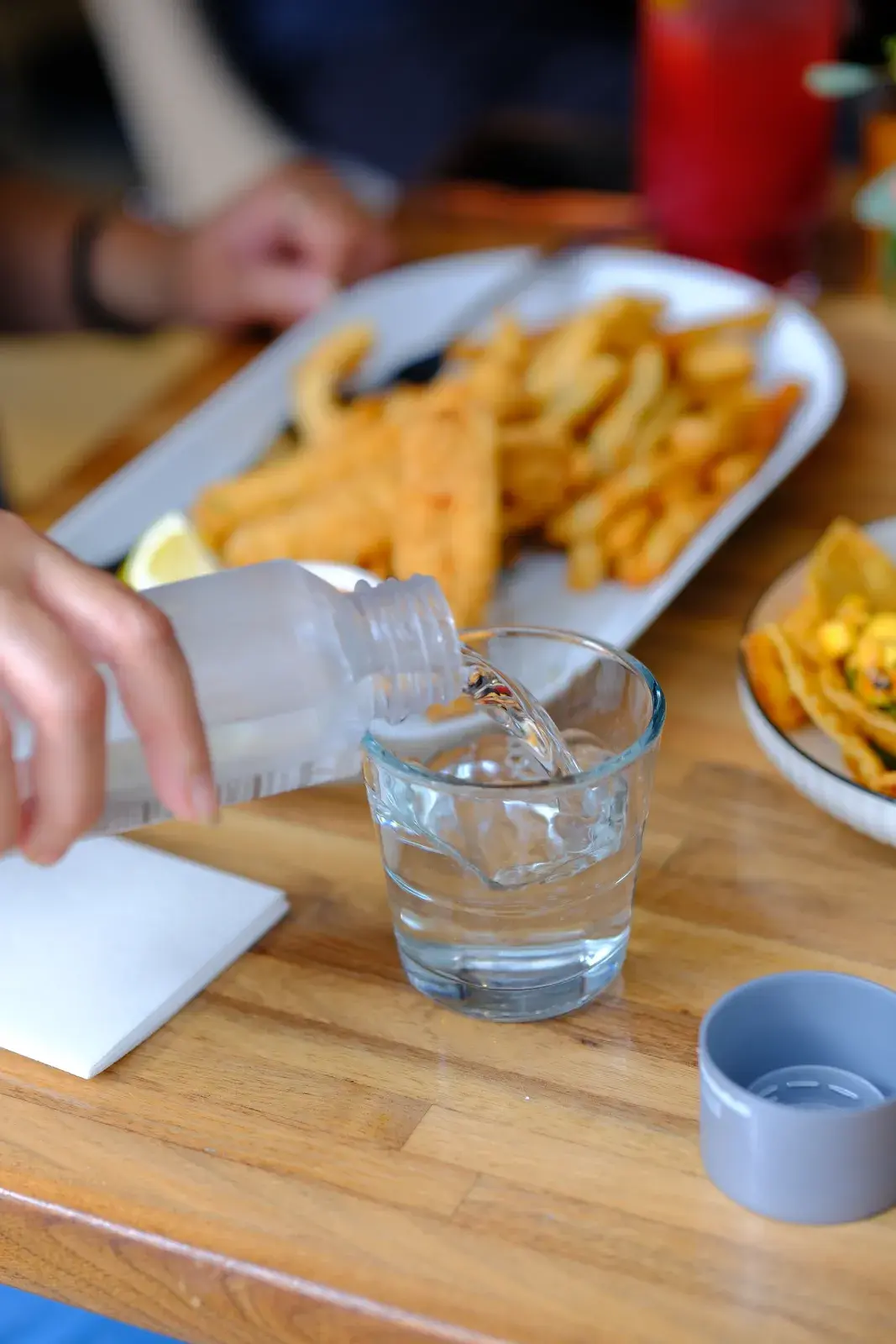 Water being poured at a table beside a plate of fish and chips
