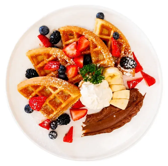 A waffle with strawberries, blackberries, banana, whipped cream and chocolate sauce