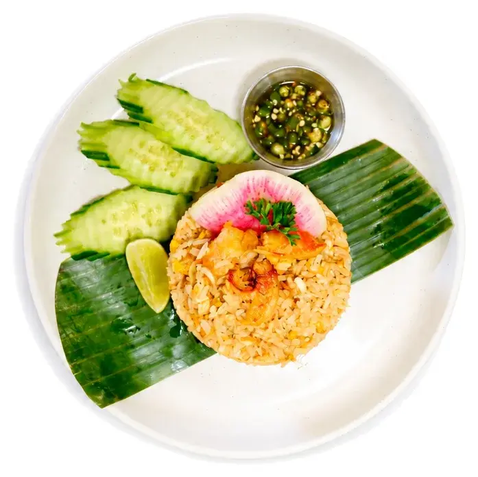 Fried rice on a banana leaf with sliced cucumber and a pot of green sauce